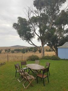 uma mesa de piquenique e cadeiras num campo com uma árvore em Wantana Cottage Farmstay em Boorowa