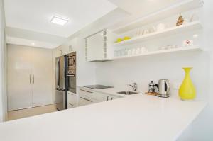 a white kitchen with white cabinets and a refrigerator at Kananda in Noosa Heads