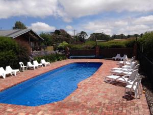 una piscina con sillas blancas y una piscina en Prom Coast Holiday Lodge, en Waratah Bay