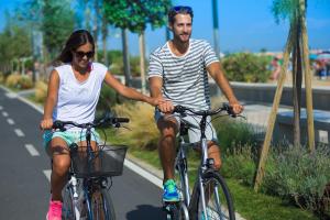a man and a woman riding bikes down a street at Laguna Grande monolocali in Bibione