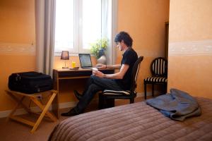 a man sitting at a desk with a laptop in a hotel room at logis hôtel Le petit breuil in La Courtine