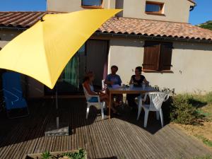 three people sitting at a table under a yellow umbrella at Un petit nid dans la garrigue in Saint-Pierre-des-Champs +3 photos