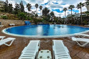 una gran piscina con sillas blancas y palmeras en Apartment Americos El Dorado, en Playa de las Américas