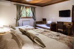 Un dormitorio con dos camas y un escritorio y un televisor. en Pousada Águia Branca, en Gramado