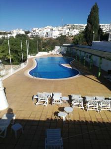 una piscina con sedie bianche e tavoli accanto a un edificio di Apartamento Varandas do Mar AL63644 ad Albufeira