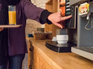 una persona está poniendo una taza en una cafetera en Hôtel Restaurant Les Alpins en Saint-Julien-en-Beauchêne