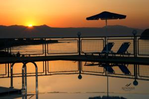 um par de cadeiras e um guarda-sol num cais com o pôr-do-sol em Renieris Hotel em Stalós