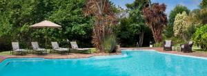 a swimming pool with chairs and an umbrella at Hunter's Country House in Plettenberg Bay