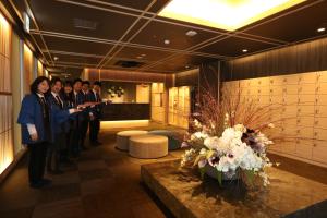 a group of people standing in a lobby with flowers at Cabin & Capsule Hotel J-SHIP Osaka Namba in Osaka