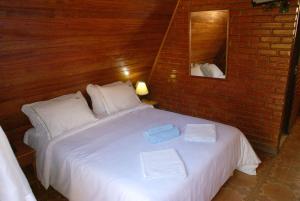 a bedroom with a white bed with a brick wall at Hotel Fazenda Caluje in Engenheiro Paulo de Frontin