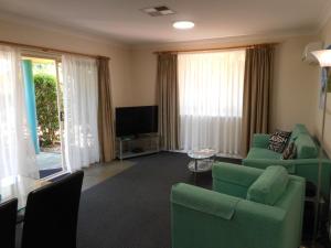 a living room with green chairs and a flat screen tv at Beaches Serviced Apartments in Nelson Bay