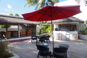 a patio with a table and chairs and a red umbrella at La Tonnelle Guest House in Trou aux Biches
