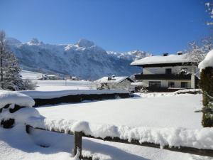 un patio cubierto de nieve con una casa y montañas en Ferienwohnung Ronacher, en Abtenau