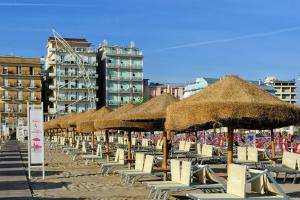 a row of straw umbrellas and chairs on a beach at Holiday Thea & Residence in Gabicce Mare