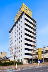 Super Hotel Izumo Ekimae في إزومو: مبنى ابيض كبير عليه علامة صفراء