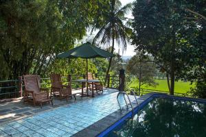 a patio with chairs and an umbrella next to a pool at Villa Sawah Resort Managed by Salak Hospitality in Bogor