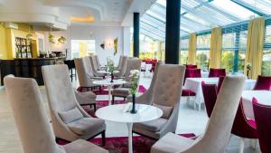 un restaurante con mesas y sillas blancas y ventanas en Royal Park Hotel & Spa, en Mielno