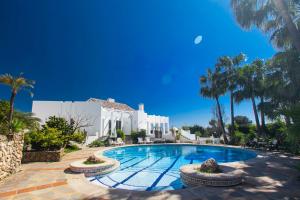 a swimming pool in front of a white building with palm trees at Villa Capricho in Marbella