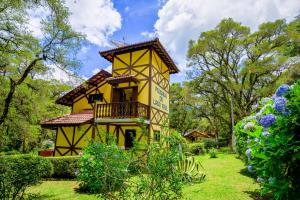 a yellow house with a balcony in a garden at Pousada Lago Azul in Monte Verde