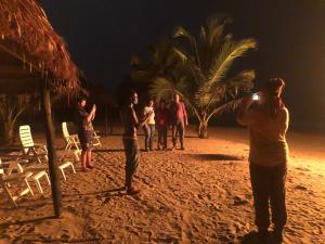 un groupe de personnes debout sur la plage la nuit dans l'établissement The Akwidaa Inn, à Akwida