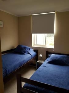 1 dormitorio con 2 camas con sábanas azules y ventana en Laguna Bahía, Algarrobo, en Algarrobo