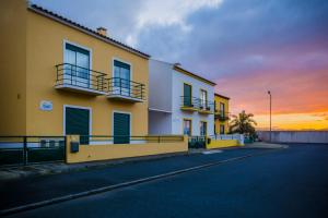 a yellow and white building with a sunset in the background at Areal de Santa Bárbara Guest House in Ribeira Grande