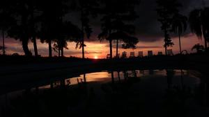 um pôr-do-sol com palmeiras e uma piscina de água em Hotel Pousada La Vierro em Ponta Grossa