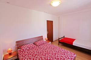 a bedroom with a bed with a red and white comforter at Apartmani Stipanelo in Murter