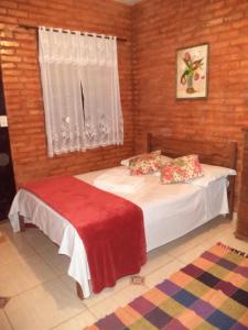 a bedroom with a bed with a red blanket and a window at Chales Recanto das Seriemas in São Roque de Minas