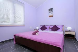 a bedroom with a large bed with pink sheets and purple pillows at D&A Apartments in Vela Luka