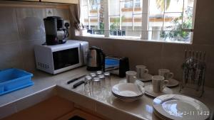 a kitchen counter with a microwave and some plates and cups at Alpha Villa - Studios without kitchen in Flic-en-Flac