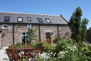 an old stone house with a table and chairs in the garden at Anniston Farm Cottages in Inverbervie