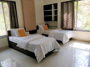 a bedroom with two beds with white sheets and orange pillows at Bauhinia in Pune