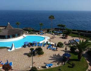 a pool with chairs and umbrellas next to the ocean at Apartamentos Rocas del Mar in Costa Del Silencio