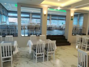 a dining room with white chairs and tables and windows at Karavan 123 in Raška
