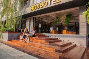 a man and woman sitting on a bench in front of a building at Bossotel Chiang Mai - SHA Plus in Chiang Mai