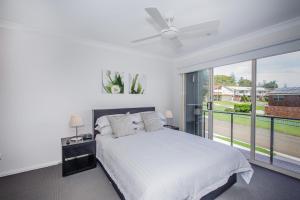 a white bedroom with a bed and a large window at Escape At Nobbys Executive Townhouse 1 74 Pacific Drive in Port Macquarie