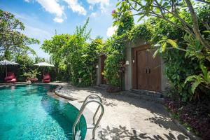 a swimming pool next to a house with a wooden door at Ladera Villa Ubud in Ubud