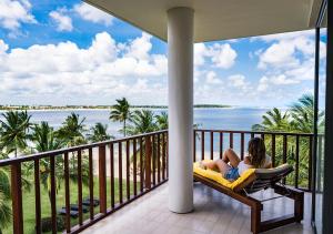 una donna seduta su una sedia su un balcone con vista sull'oceano di Amaya Beach Passikudah a Pasikuda