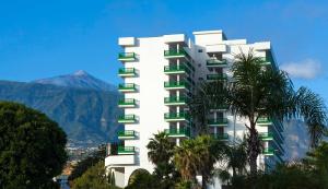 a white building with green windows and a mountain at Sol Puerto de la Cruz Tenerife in Puerto de la Cruz