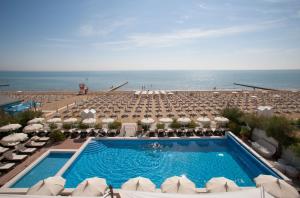 een zwembad met parasols en stoelen en de oceaan bij Hotel Delle Nazioni in Lido di Jesolo