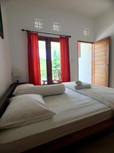 a bedroom with two beds with red curtains and a window at Uluwatu Made Guesthouse in Uluwatu