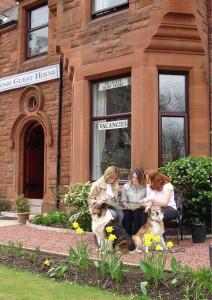 um grupo de mulheres sentadas num banco com dois cães em Ferintosh Guest House em Dumfries