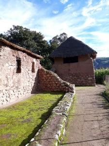 a stone building with a thatched roof next to a stone wall at Hostal Ayllu in Urubamba