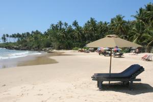 a beach with a chair and an umbrella on the sand at Saman Homestay in Tangalle
