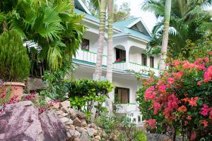 a white house with palm trees and flowers in front of it at Evergreen Apartments in Anse Boileau
