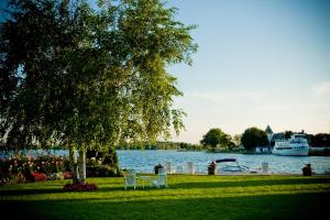 a park with a tree and a boat in the water at The Gananoque Inn & Spa in Gananoque