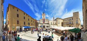 a crowd of people walking around a street with a clock tower at Main Street Studio and Rooms in Zadar