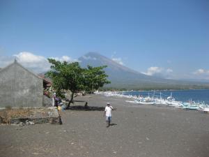 a man standing on a beach with boats on the water at Bubu Racok Homestay in Amed