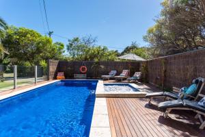 a swimming pool with chairs and a wooden deck at Front Beach House in Blairgowrie